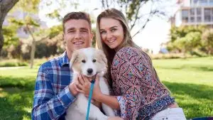 Happy couple holding a white puppy on a leash in a sunny park