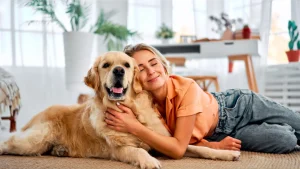 Woman smiling and hugging a Golden Retriever dog on the floor in a bright living room